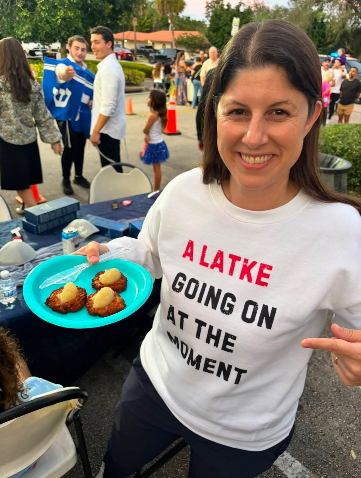 Leah Grossman wearing the A Latke Going On at the Moment T-shirt while serving latkes.