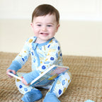 Smiling baby wearing the Latkes & Light Hanukkah Zippy while holding a book, with convertible feet folded closed.