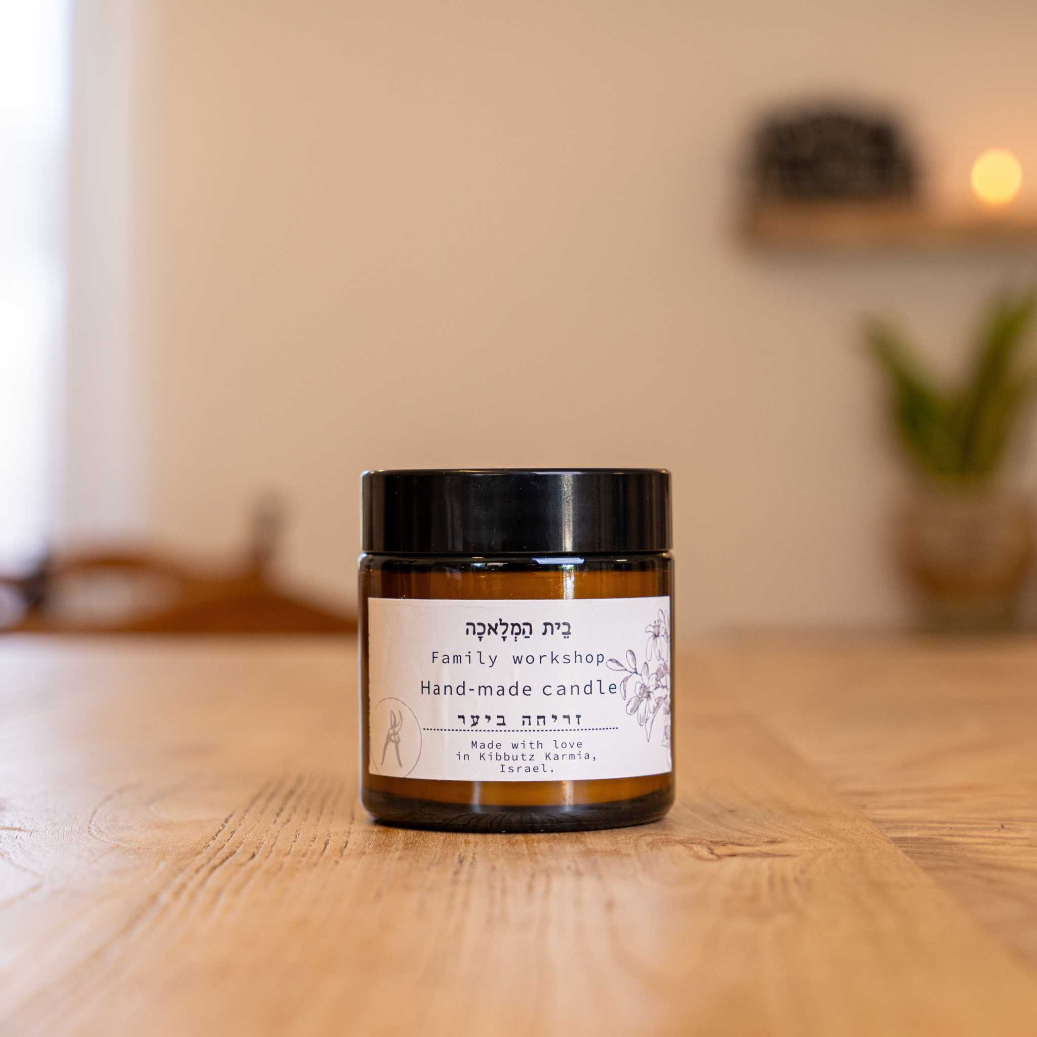 Israeli beeswax candle by Beit HaMelacha in an amber glass jar on a wooden table