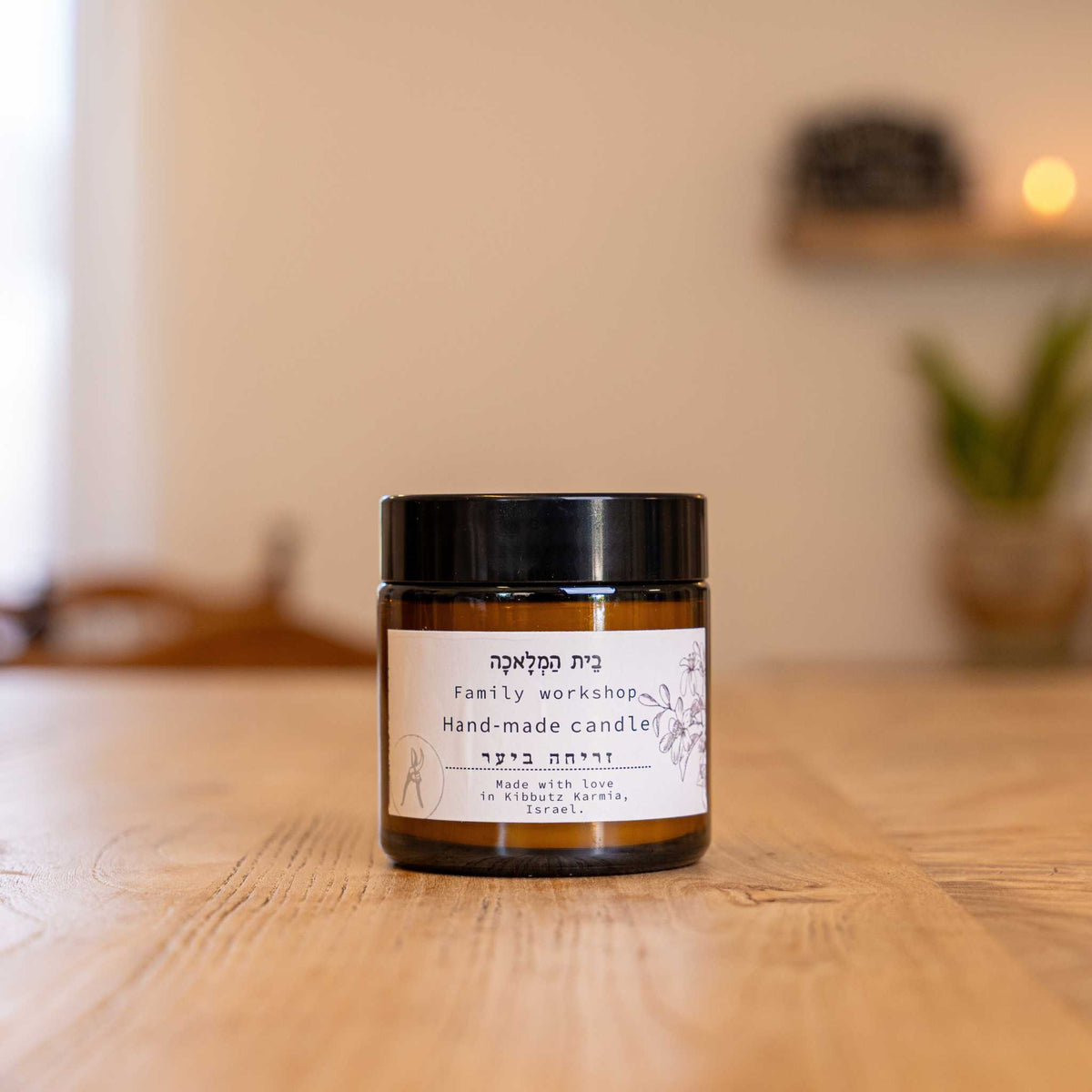 Israeli beeswax candle by Beit HaMelacha in an amber glass jar on a wooden table