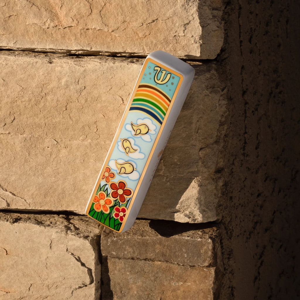 Bright Beginnings rainbow and floral ceramic mezuzah mounted on a stone doorway