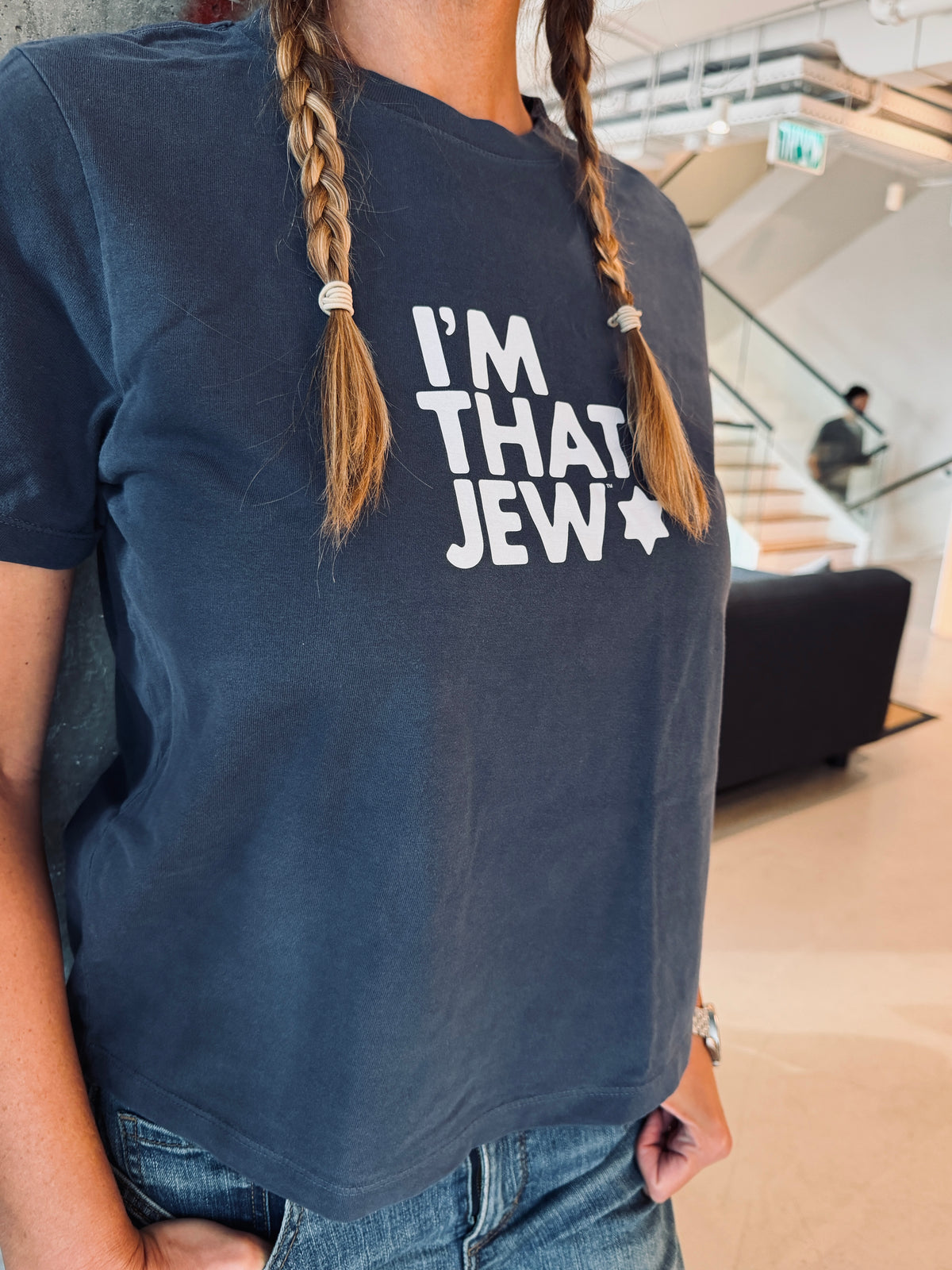 Dina Chitayat wearing a faded navy women's garment-dyed I'm That Jew T-shirt with white lettering and a Star of David, styled with blue jeans.