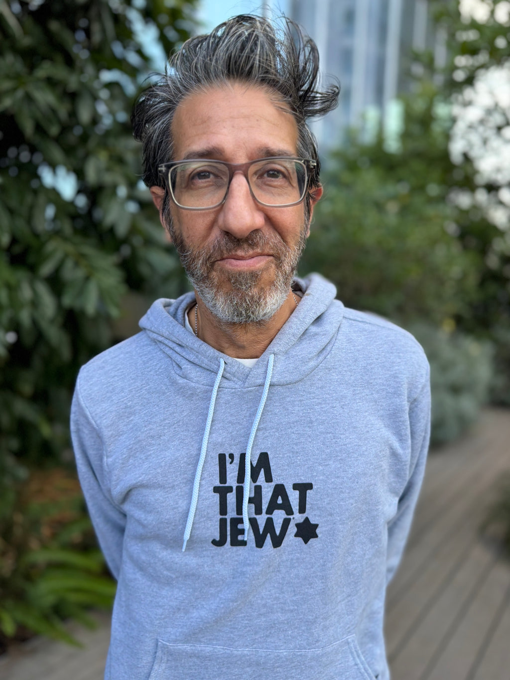 Eitan Chitayat wearing a heather gray I'm That Jew pullover hoodie with black lettering and a Star of David, photographed outdoors.