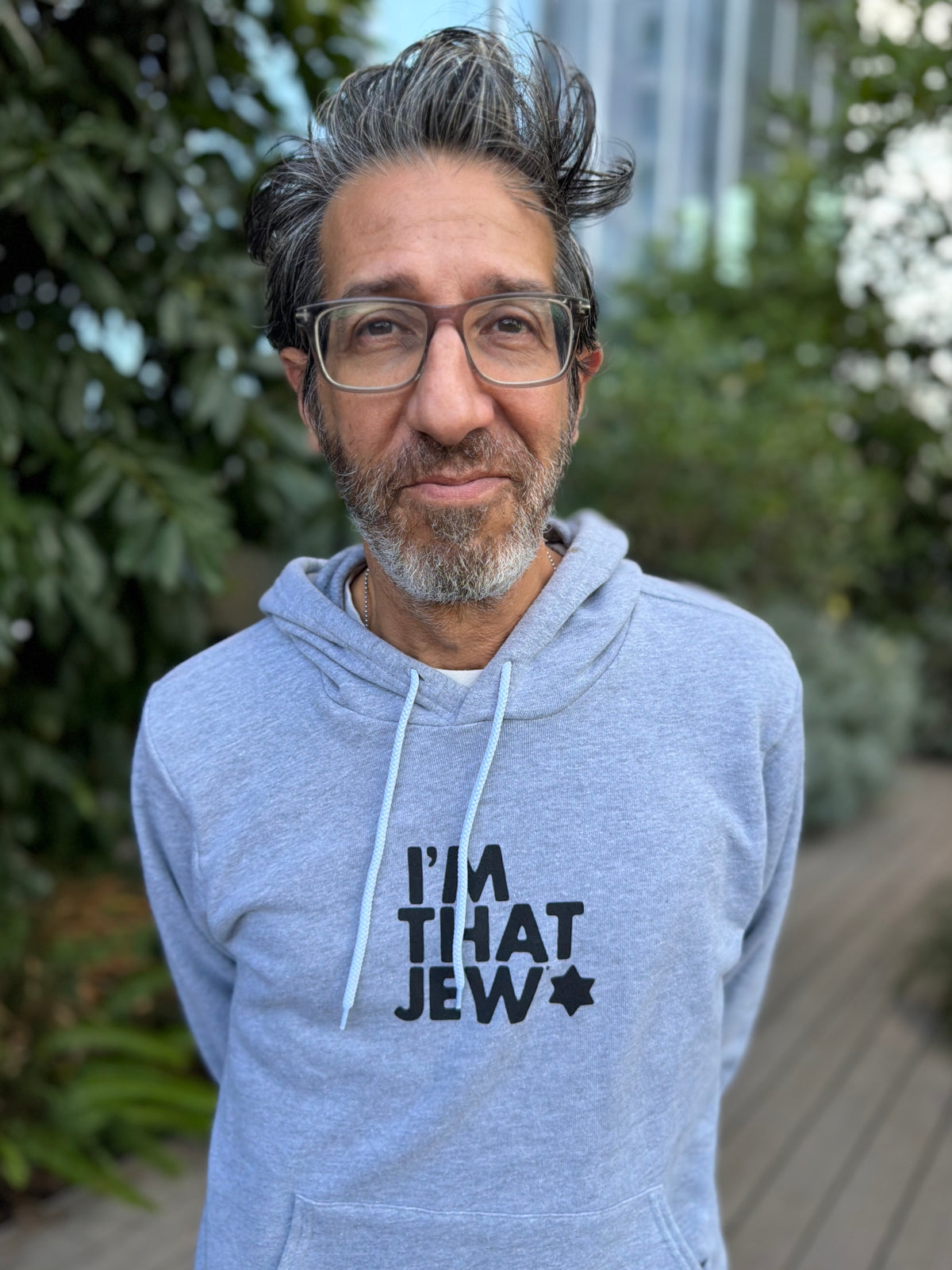 Eitan Chitayat wearing a heather gray I'm That Jew pullover hoodie with black lettering and a Star of David, photographed outdoors.