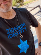 Eitan Chitayat wearing a black ZIONisM Identity T-shirt with blue lettering and a large blue Star of David graphic, photographed outdoors.