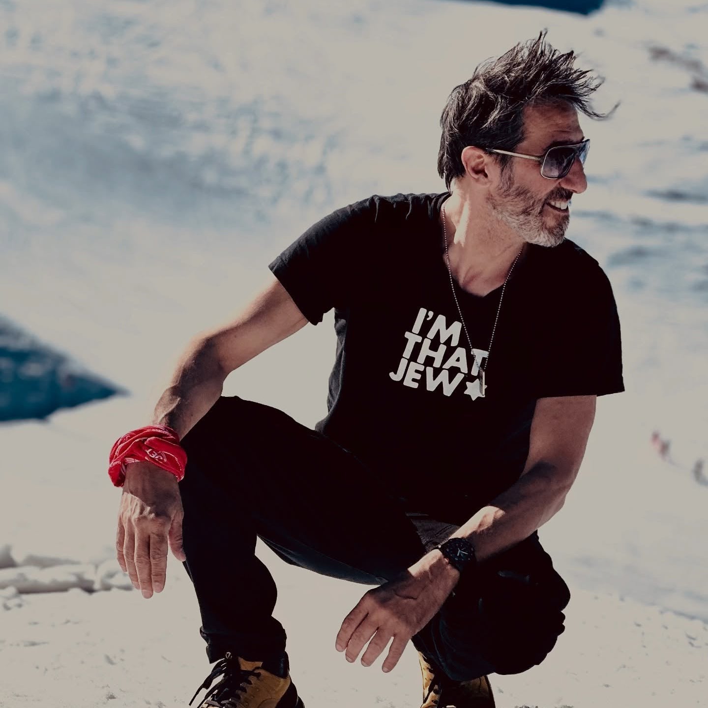 Man squatting in a snowy landscape wearing a black t-shirt with text.
