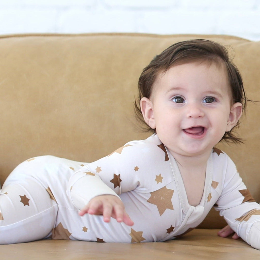 Baby wearing the Golden Hour Hanukkah Zippy with neutral gold Star of David print.