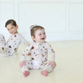 Smiling toddler wearing Golden Hour Hanukkah Zippy with gold Star of David print, with a child in matching pajamas behind.