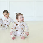 Smiling toddler wearing Golden Hour Hanukkah Zippy with gold Star of David print, with a child in matching pajamas behind.