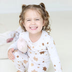 Smiling girl wearing Golden Hour Hanukkah two-piece pajamas with gold Star of David print.