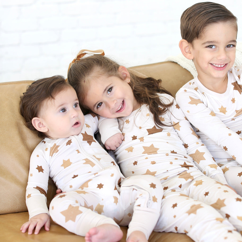 Three children wearing matching Golden Hour Hanukkah pajamas with gold Star of David print.