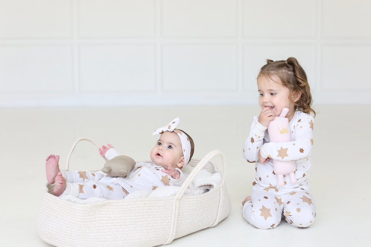 Baby and toddler wearing matching Golden Hour Hanukkah pajamas with gold Star of David print.