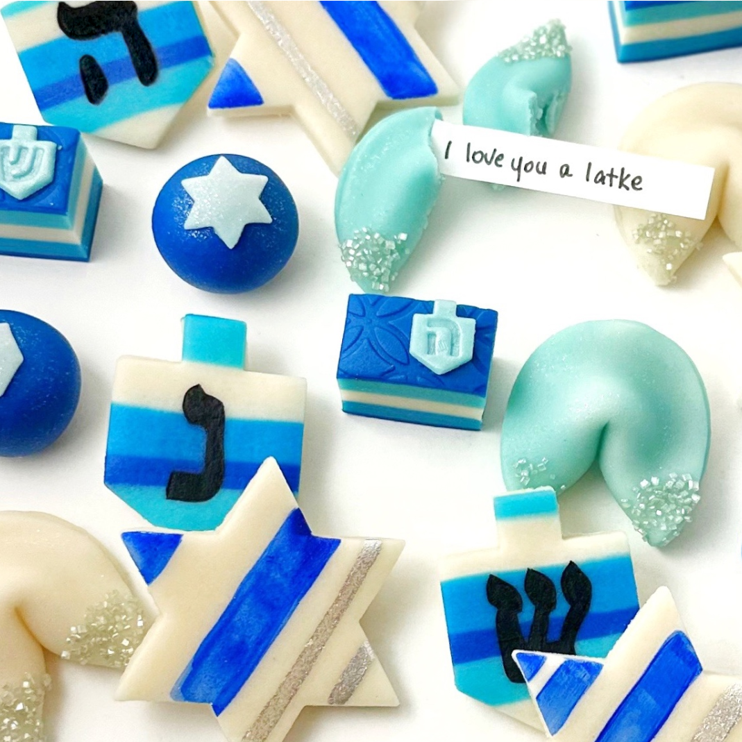 Close-up of Hanukkah marzipan treats including dreidels, Stars of David, and a fortune cookie with an “I love you a latke” message.
