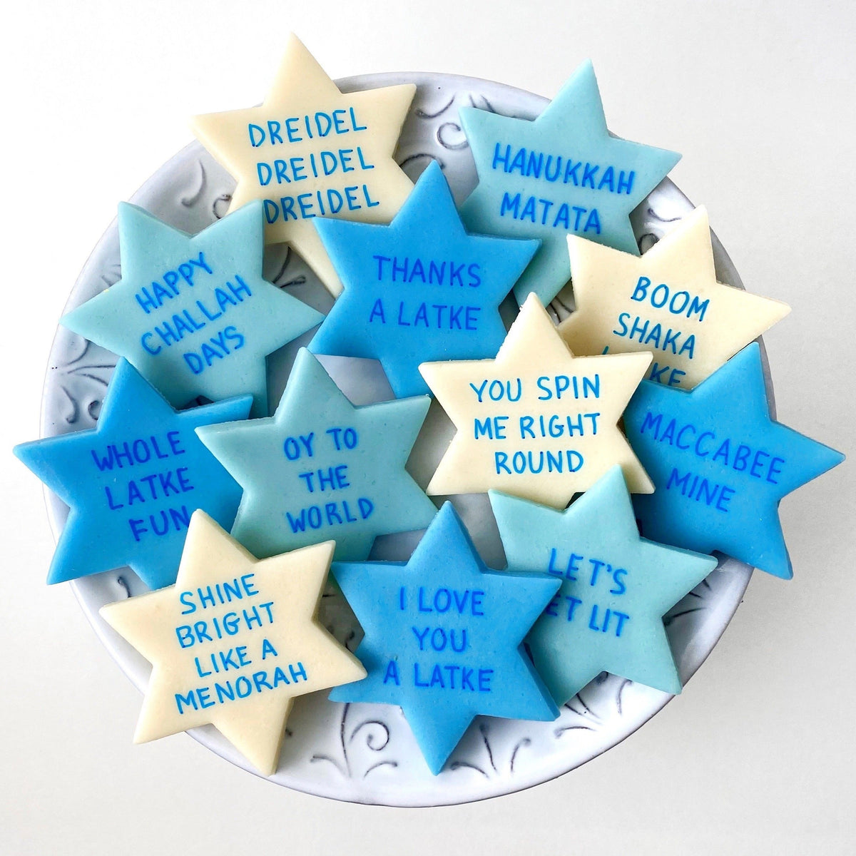 Blue, aqua, and cream Star of David marzipan conversation tiles featuring playful Hanukkah sayings arranged on a serving plate.