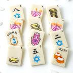 Hanukkah marzipan mahjong tiles hand-painted with menorahs, gelt, dreidels, hamsas, sufganiyot and Stars of David.