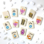 Hanukkah marzipan mahjong tiles arranged with menorahs, gelt, Stars of David, a dreidel, hamsa and sufganiyot designs.
