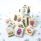 Hanukkah marzipan mahjong tiles styled around a cup with hand-painted dreidel, menorah, gelt, hamsa, Star of David and sufganiyot designs.