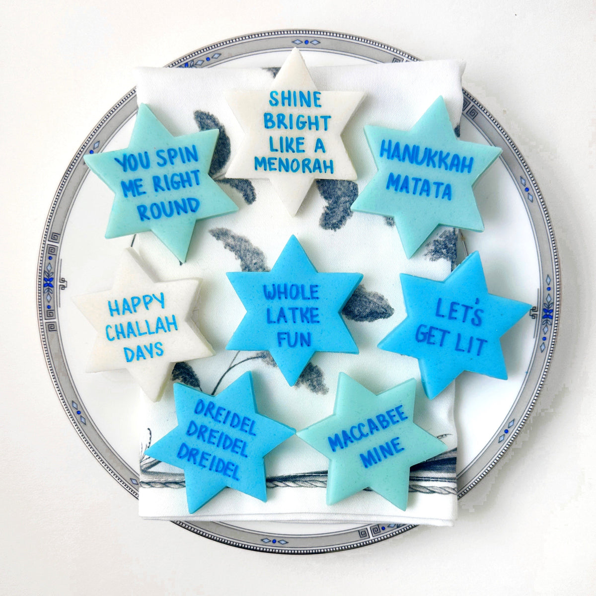 Star of David marzipan conversation tiles in blue, aqua, and cream with playful Hanukkah sayings arranged on a serving plate.