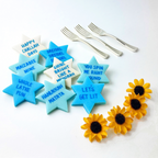Blue, aqua, and cream Star of David marzipan conversation tiles with playful Hanukkah sayings arranged with silver forks and yellow flowers.