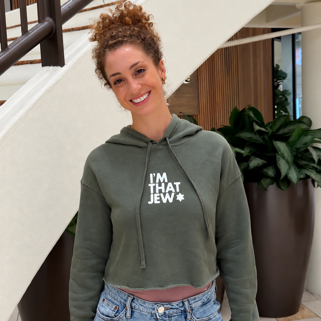 Monica Czukerberg wearing the olive green I'm That Jew cropped hoodie with white lettering, styled with blue jeans.