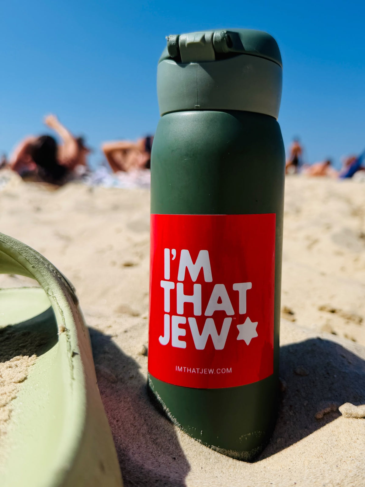 Red I'm That Jew sticker with white lettering and a Star of David on a green reusable water bottle at the beach.