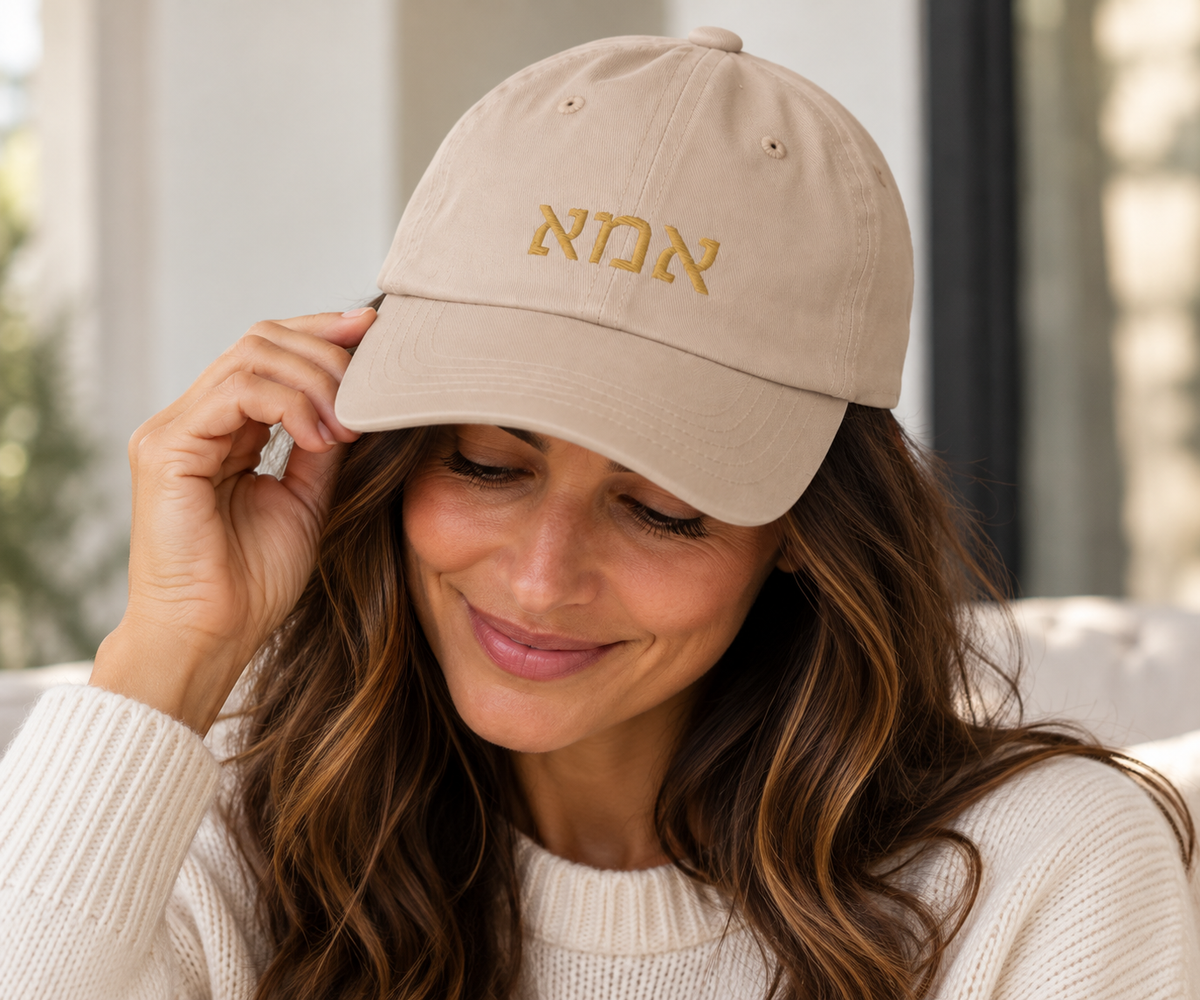 Woman wearing a stone Ima (אמא) dad hat with gold Hebrew embroidery and a cream knit sweater.