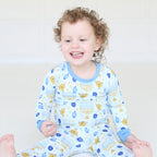 Smiling toddler wearing the Latkes & Light Hanukkah two-piece set with menorah, dreidel and latke print.