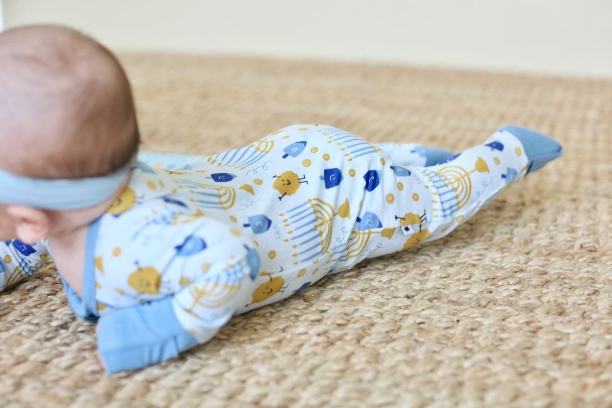 Back view of baby wearing the Latkes & Light Hanukkah Zippy with menorah, dreidel and latke print.