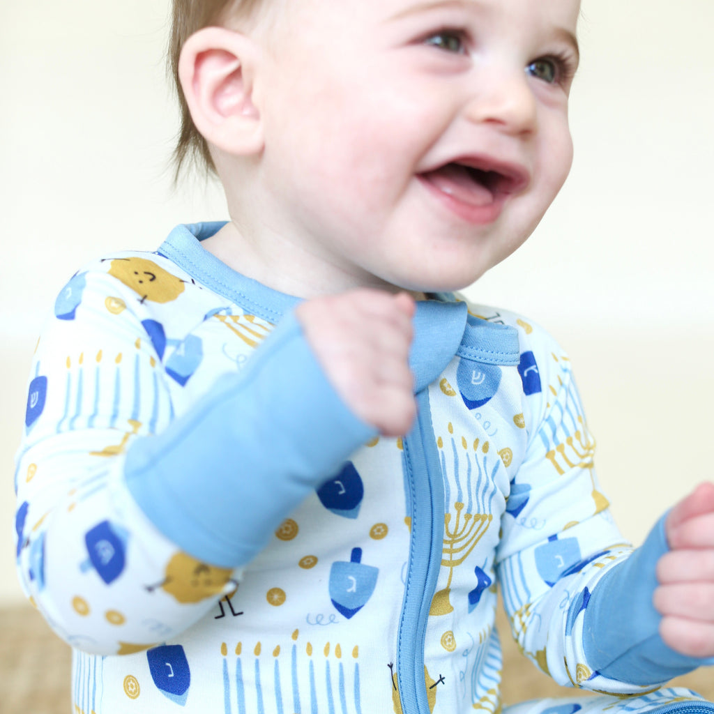 Close-up of baby wearing the Latkes & Light Hanukkah Zippy with blue zipper and menorah, dreidel and latke print.
