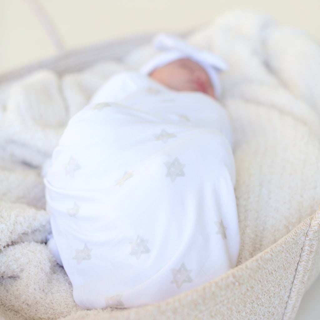 Newborn resting in a basket wrapped in the neutral Magen Dreams Star of David swaddle