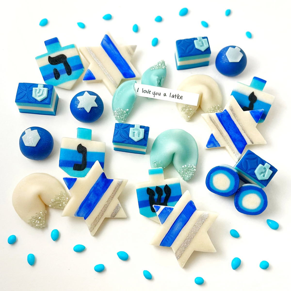 Assortment of blue and white Hanukkah marzipan treats including dreidels, Stars of David, rainbow cookies, and fortune cookies