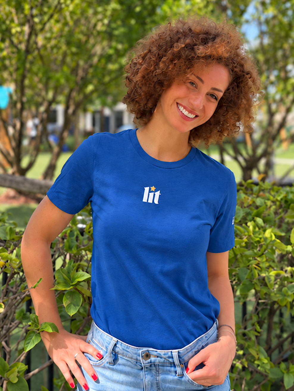 Monica Czukerberg wearing a royal blue Lit T-shirt with a small multicolored Hebrew-inspired graphic on the chest, standing outdoors with her hands in her jeans pockets.