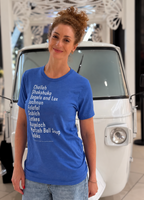 Monica Czukerberg wearing a blue The Ten Jewish Foods T-shirt featuring a list of Jewish dishes in white lettering, standing in front of a vintage white vehicle.