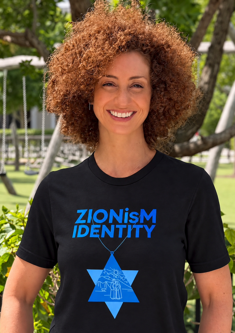 Monica Czukerberg wearing a black ZIONisM Identity T-shirt with bright blue lettering and a Star of David graphic, standing outdoors.