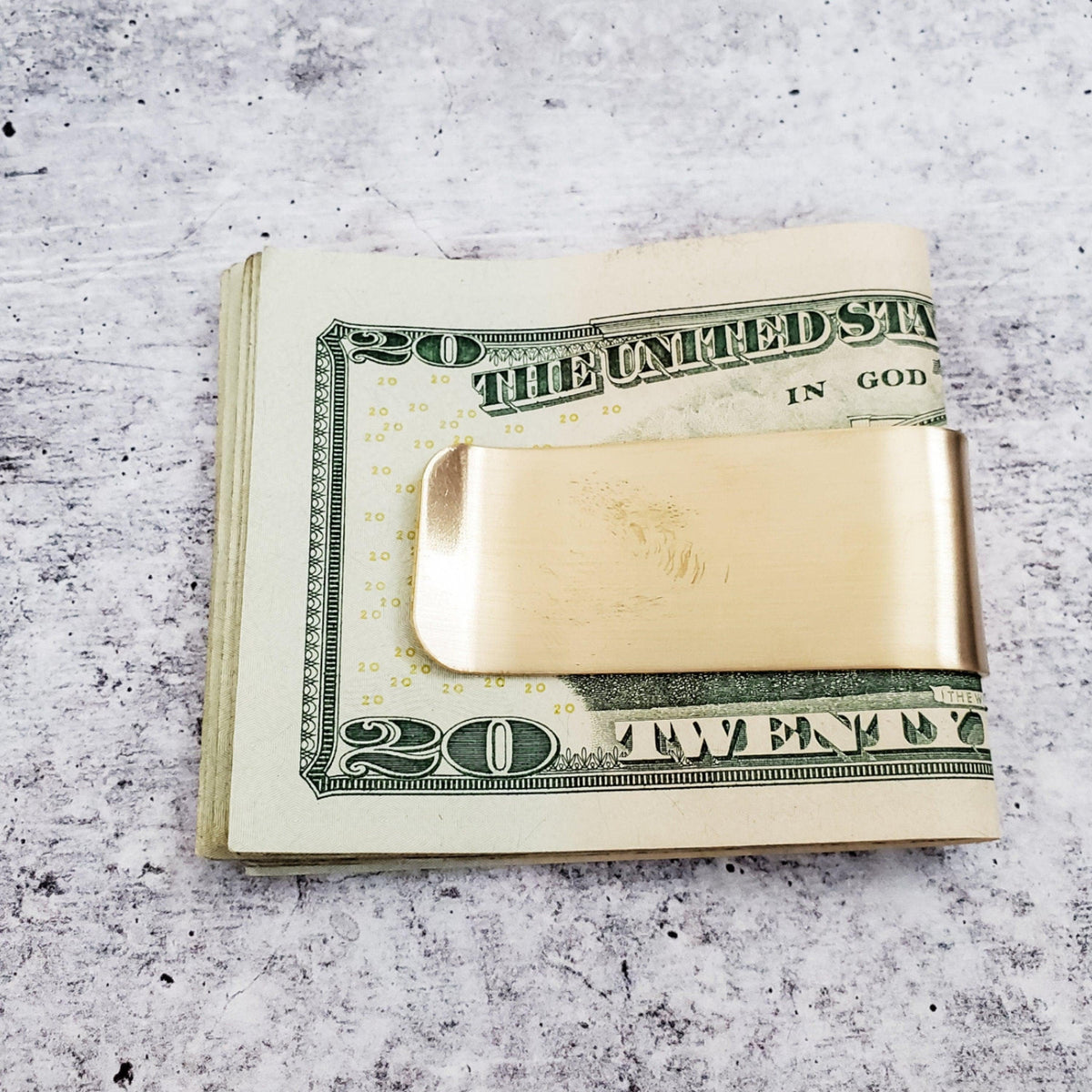 Yellow brass Nice Jewish Boy money clip holding a folded stack of twenty-dollar bills, showing how the clip secures cash.