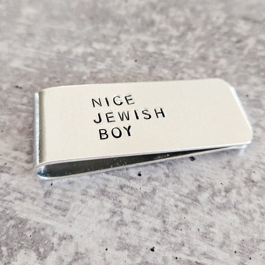 Angled view of the silver NICE JEWISH BOY money clip, showing the hand-stamped lettering and polished metal finish.