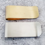Back view of two handmade money clips in yellow brass and silver finishes, showing their smooth metal surfaces and folded edges.