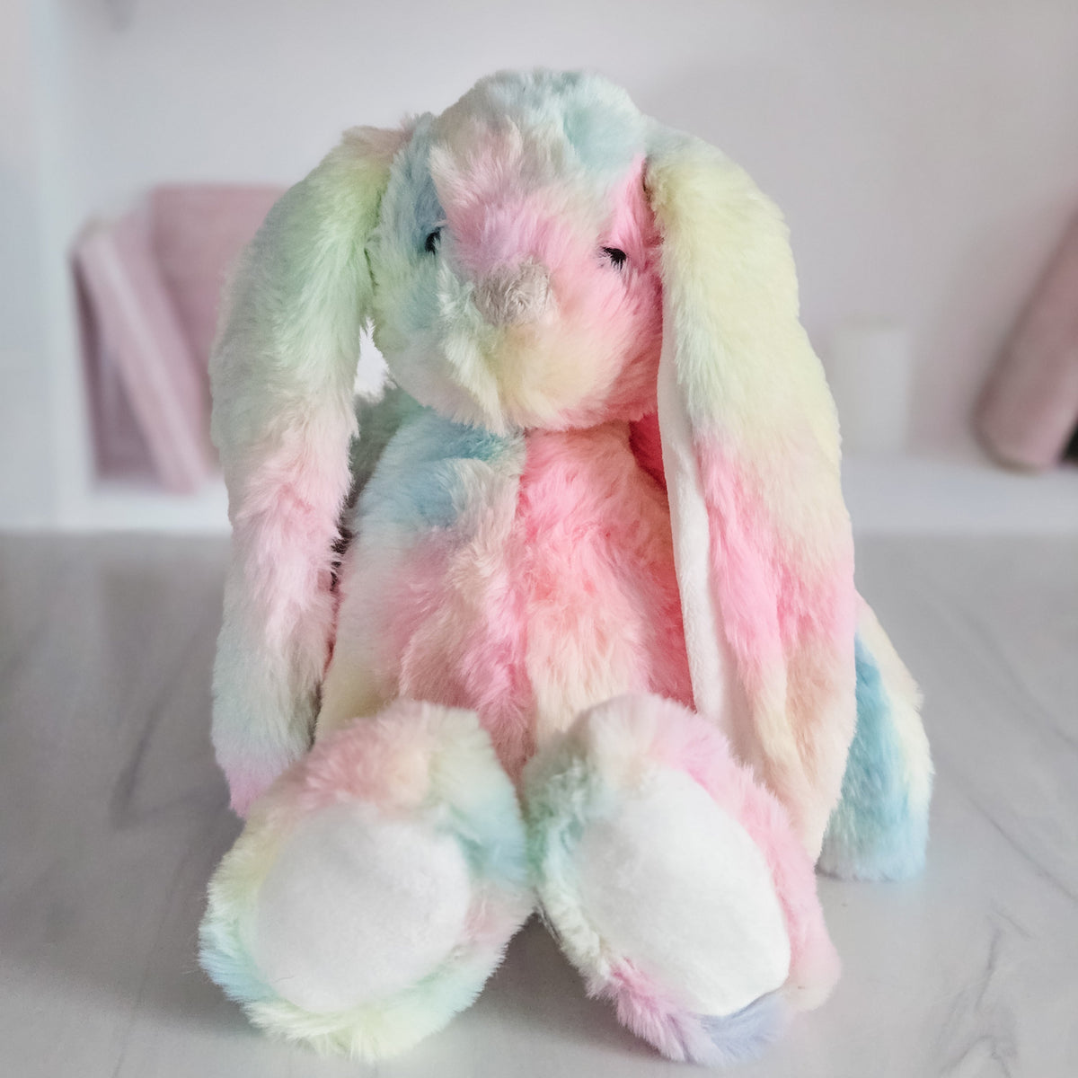 Rainbow plush bunny with pastel pink, blue, green and yellow fur and long floppy ears