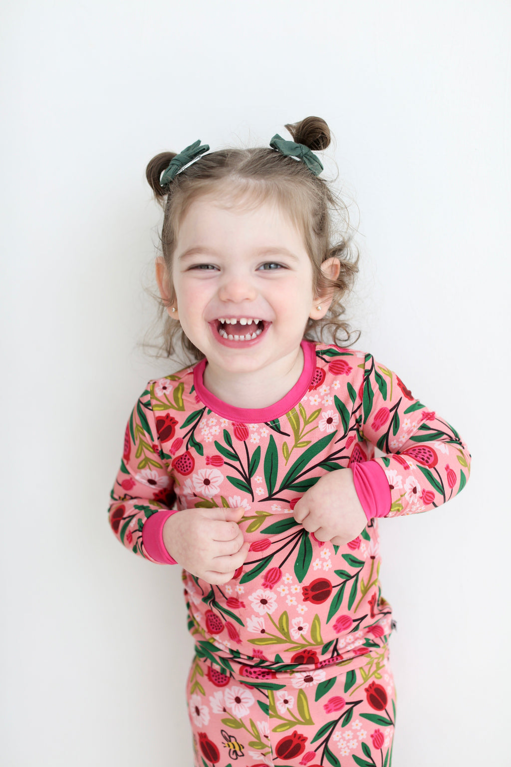 Smiling girl wearing pink Petals & Pomegranates pajamas with pomegranates, flowers and tiny honeybees