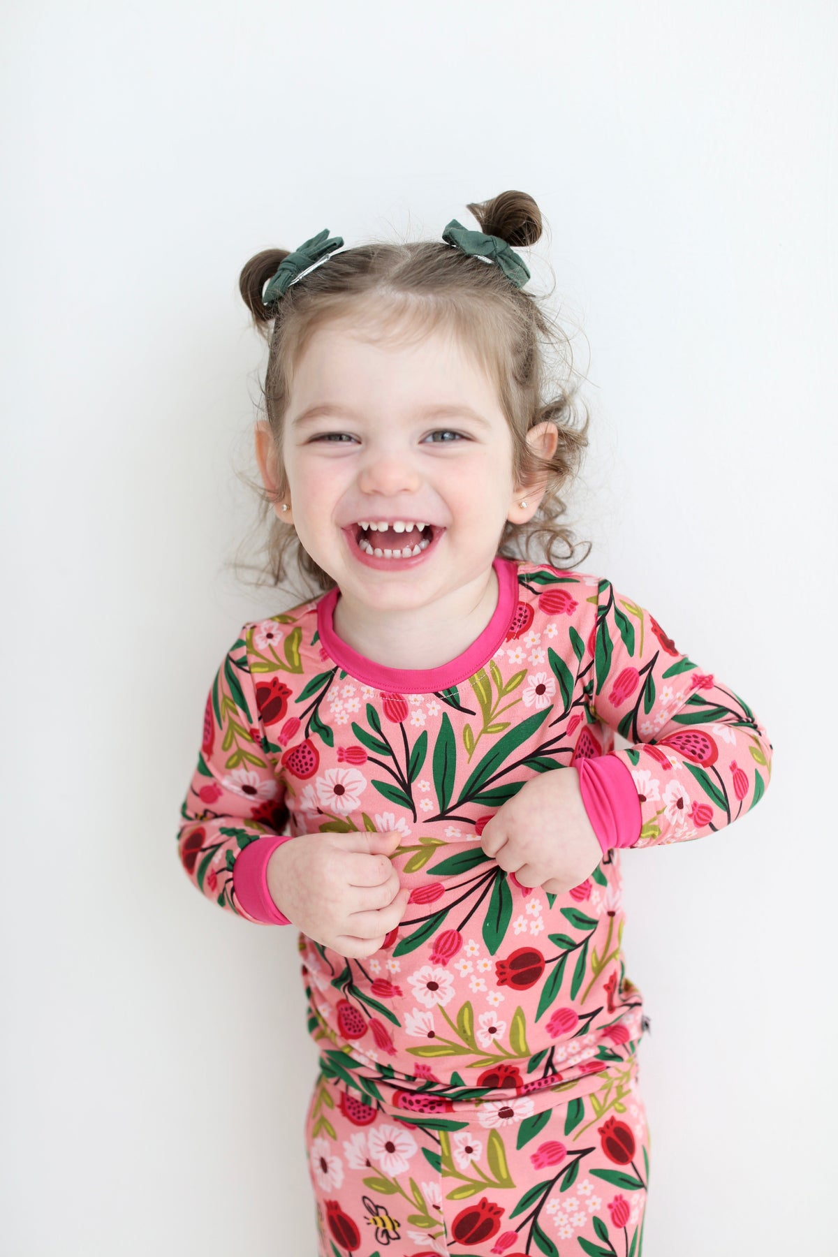 Smiling girl wearing pink Petals & Pomegranates pajamas with pomegranates, flowers and tiny honeybees