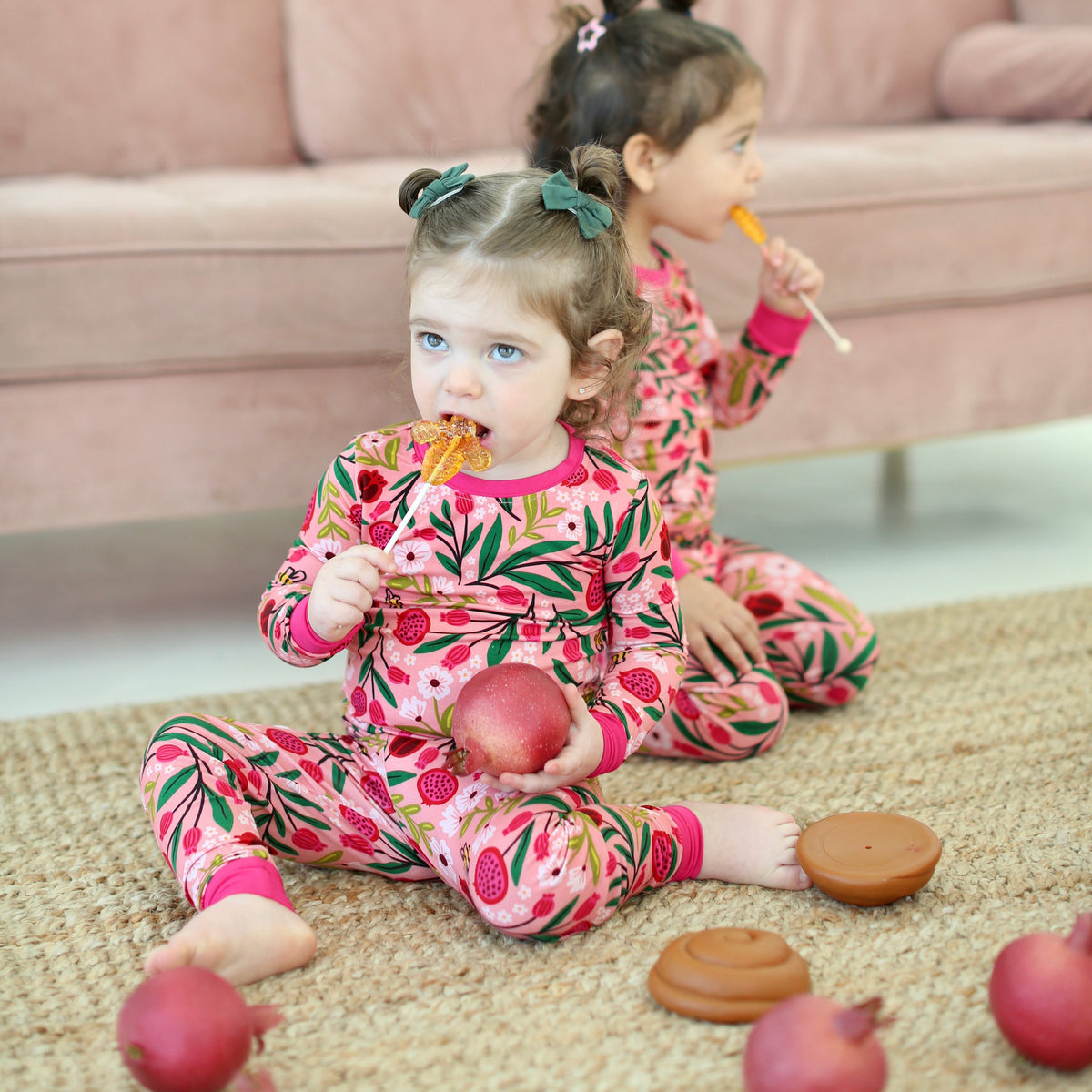 Two girls in matching Petals & Pomegranates pajamas sitting with apples for Rosh Hashanah