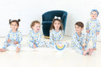 Five children wearing Shiloh & Kate Latkes & Light Hanukkah pajamas gathered around a rainbow menorah.