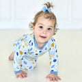 Toddler crawling in Shiloh & Kate Latkes & Light Hanukkah pajamas with blue trim and menorah, dreidel, and latke illustrations.