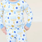 Close-up of Latkes & Light two-piece Hanukkah pajamas with blue trim and menorah, dreidel, and latke illustrations.