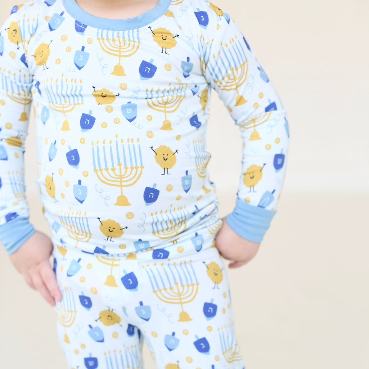 Close-up of Latkes & Light two-piece Hanukkah pajamas with blue trim and menorah, dreidel, and latke illustrations.
