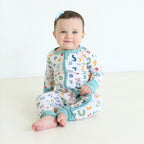Smiling baby wearing Shiloh & Kate Aleph Bet zip-up pajamas featuring colorful Hebrew letters on a white background with soft teal trim.
