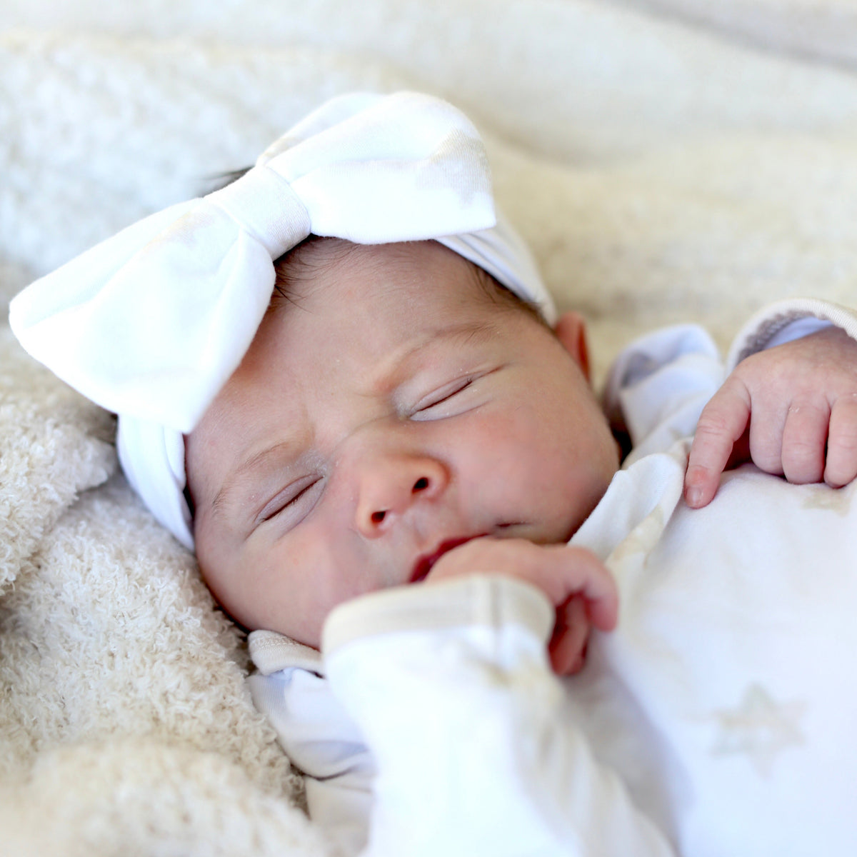 Sleeping newborn wearing a white bow headband and Star of David pajamas by Shiloh & Kate.
