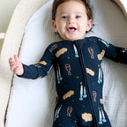 Smiling baby wearing Shiloh & Kate Navy Shabbat zip-up pajamas with challah, Kiddush cups, and Shabbat candles on a dark navy background.