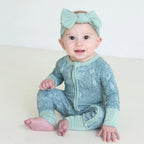 Smiling baby wearing Shiloh & Kate Sage Bloom zip-up pajamas with a delicate floral print, mint green trim, and a matching bow headband.