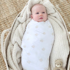 Newborn wrapped in a white Shiloh & Kate swaddle blanket with a soft gold Star of David print, resting on a cozy cream blanket.